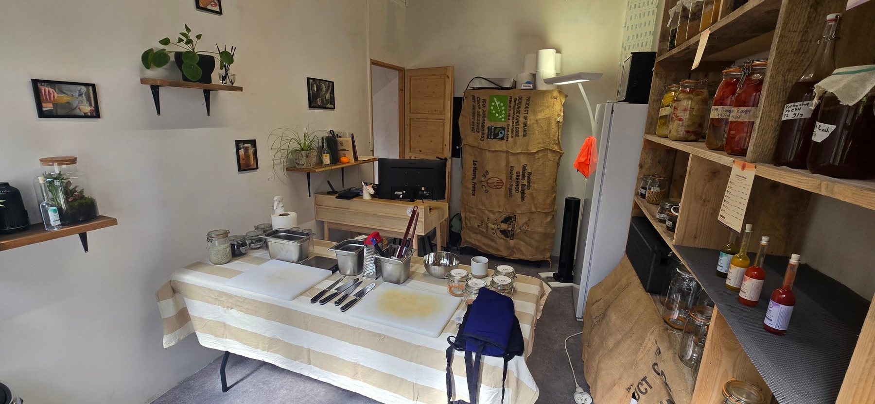 Le lieu un jour d'atelier : la grande table installée avec planches et couteaux, devant les étagères de bocaux en fermentation
