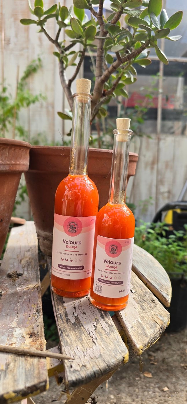 Deux bouteilles de sauce pimentée fermentée « Velours Rouge » posées sur une table en bois