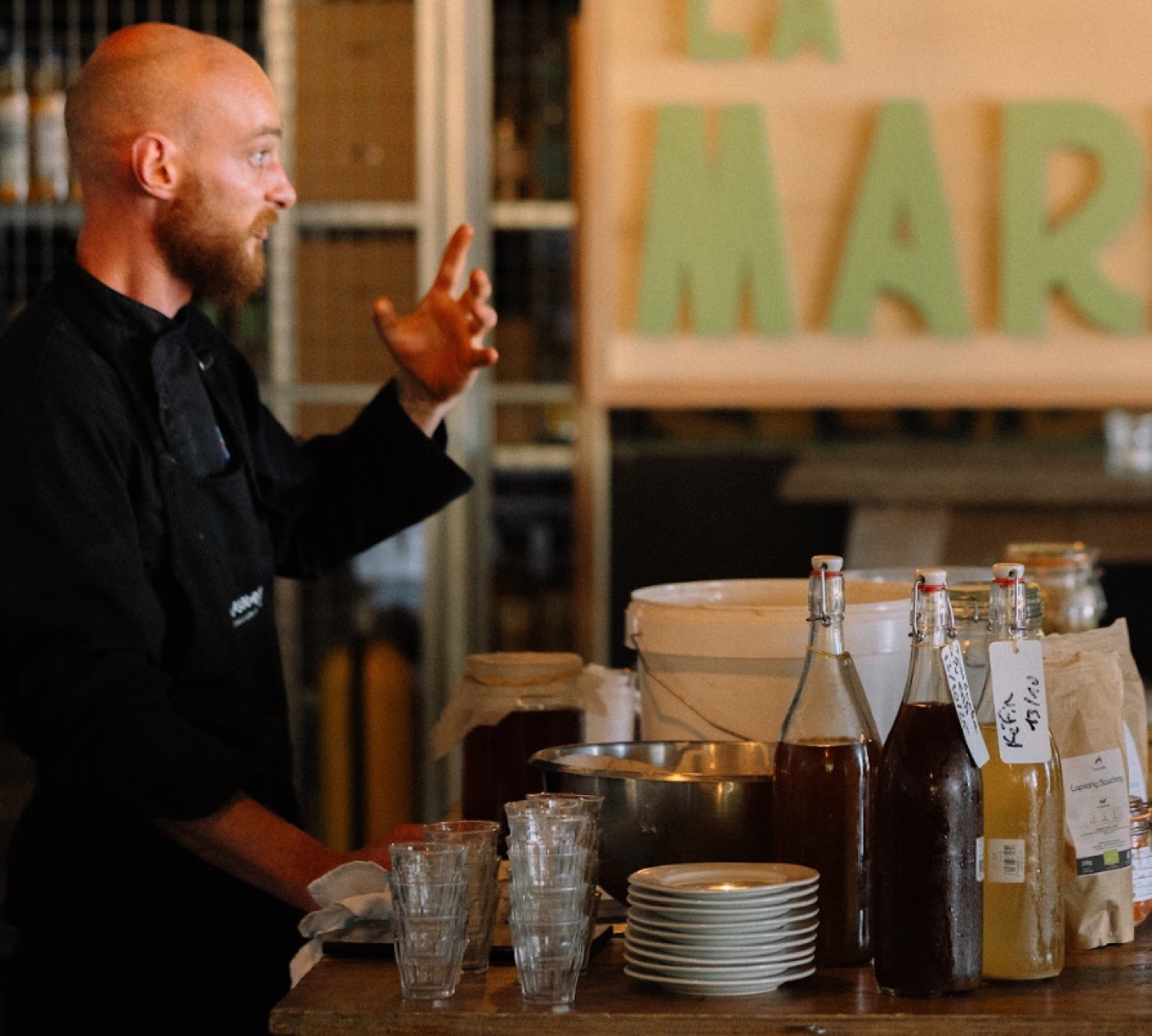 Nicolas en démonstration de fermentation au marché, entouré de bocaux et bouteilles